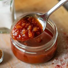 a spoon full of sauce sitting on top of a wooden cutting board next to some spices