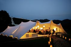 a group of people standing in front of a white tent with lights on it at night