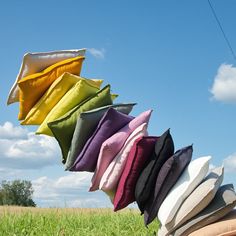 several different colored pillows hanging from a line in the grass with a blue sky behind them