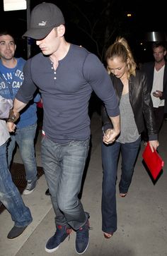 a man and woman walking down the street at night with other people in the background