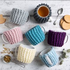 crocheted coffee mug cozyies and spoons on a white wooden table with cookies