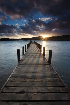 the sun is setting on a dock in the water