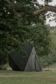 a black triangular structure sitting in the middle of a field next to a large tree