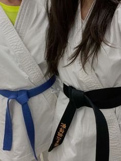 two women in white kimonos standing next to each other with black and blue belts