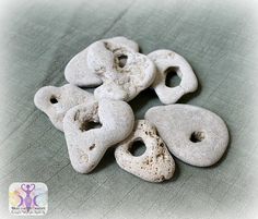 five white rocks with holes in them on a gray clothed surface, one has been cut into smaller pieces