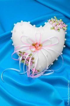 a white heart shaped pillow with pink flowers on it sitting on a blue satin background