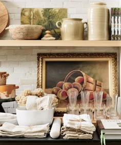 a shelf filled with dishes and glasses on top of a wooden table next to a painting