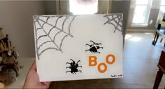 a hand holding up a halloween card with spider webs on it and boo written in orange