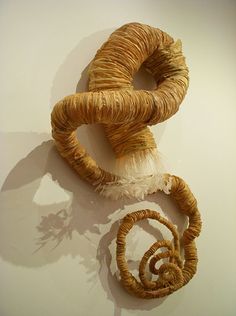 two pieces of art made out of yarn on a white wall with shadow from it