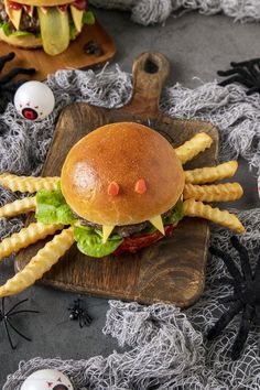 a large hamburger with fries on a wooden cutting board next to halloween decorations and fake eggs