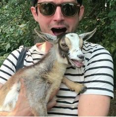 a man holding a goat in his arms and wearing sunglasses on it's head