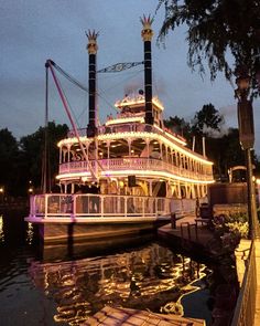 a large white boat floating on top of a river next to a dock at night