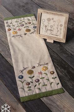 two towels with embroidered flowers on them sitting next to a framed picture and snowflake