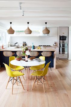 a kitchen with white walls and wooden floors, yellow chairs around a round dining table