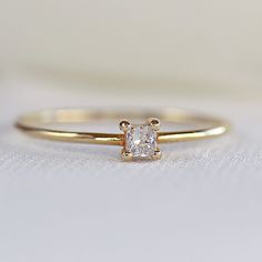 a yellow gold ring with a princess cut diamond in the center on a white surface