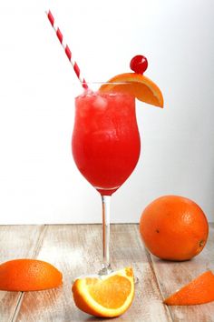 an orange cocktail garnished with cherries on a wooden table next to sliced oranges