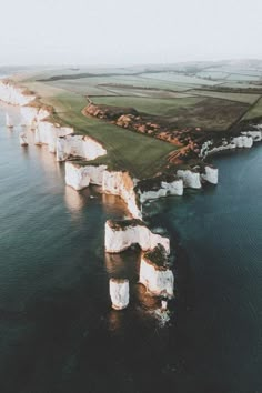 an aerial view of white cliffs in the ocean with green grass and water around them