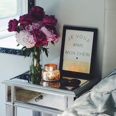 a vase with flowers on top of a mirrored table next to a mirror and candle