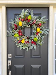 a wreath on the front door of a house decorated with fruit and greenery for christmas