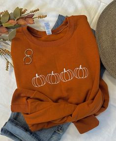 Cool Fall days and Pumpkin Patches, that's what we love!  The days become shorter but they sure seem to slow down.  Our simple pumpkin outline crew in the beautiful burnt orange is the perfect way to show you love the season in perfect minimalist style.  You will stay cozy and warm while looking super cute!   Pair with your favorite jeans, or size up one and grab your comfy leggings!  Features: 50% USA cotton, 50% polyester Pill-resistant air jet yarn Made with 50% sustainably and fairly grown U Fall Graphic Sweatshirt, Pumpkin Embroidery Designs, Embroidered Halloween Sweatshirt, Cute Fall Sweatshirts, Fall Embroidered Sweatshirts, Fall Sweatshirt Ideas, Fall Pullovers, Simple Fall Style, Autum Outfit