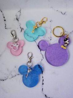 three mickey mouse keychains are on a marble counter top, one is blue and the other is pink