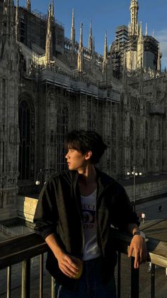 a young man standing next to a railing in front of a large castle like building