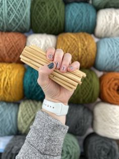 a woman holding up several skeins of yarn in front of colorful balls of yarn