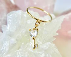 This gorgeous 14k gold-filled cubic zirconia heart key charm ring is made with your choice of a 2mm textured, 2mm smooth or 1mm thin band.  This beautiful charm measures 15x5mm.  ✦100% handcrafted ✦ High quality 14K gold filled  ✦ Ring arrives in either a pink microfiber suede envelope/pouch or a blue/green drawer cardboard box as seen in the last image of this listing. ✦ Ready to ship in one business day ✦ Average shipping time in the U.S. is three to five business days ✦ Tracking available ✦CZ heart key charm Size--15mmx5mm Color--gold Material--14k gold filled  ✦Band Style--1mm thin, 2mm smooth or 2mm textured band Color--gold  Material--14k gold filled metal ✦Size 4, 5, 6, 7, 8 ✦Don't know your ring size? Please don't guess.   Wrap a thin strip of paper around your finger like a ring ( Green Drawer, Dangle Ring, Ring With Heart, Envelope Pouch, Charm Ring, Dainty Gold Rings, Heart Key, Romantic Jewellery, Heart And Key