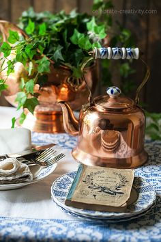 a tea kettle sitting on top of a blue and white table cloth next to a plate