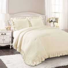 a white bed in a bedroom next to a window with flowers on the side table