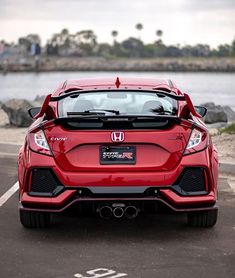 the rear end of a red honda civic hatchback parked in a parking lot next to water