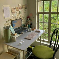 a laptop computer sitting on top of a desk next to a green chair and window