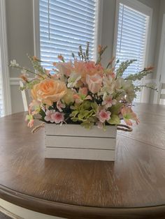 a wooden table topped with a white vase filled with flowers and greenery on top of it