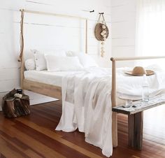 a bed with white sheets and pillows in a room next to a wooden bench on a hard wood floor