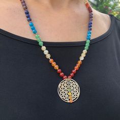 a woman wearing a necklace with a tree of life pendant and multicolored beads