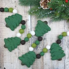 some felt christmas trees are hanging on a wooden table with pine cones and balls around them