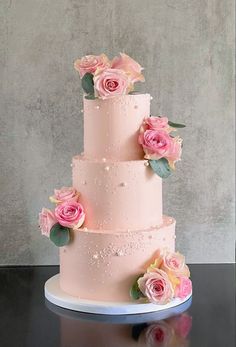 a three tiered wedding cake with pink roses on top and greenery around the edges