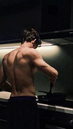 a man with no shirt is cooking in the kitchen and his back turned to the camera