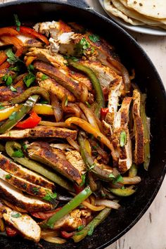 a skillet filled with chicken and vegetables on top of a wooden table next to pita bread