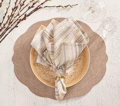 a plate with some napkins on top of it next to wine glasses and branches