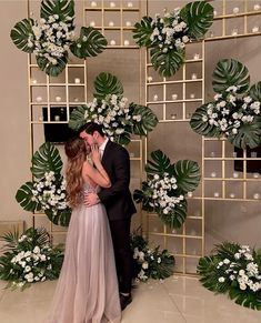 a man and woman are kissing in front of a backdrop with white flowers on it