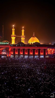 a large group of people standing in front of a building with lights on it at night