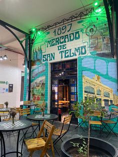 tables and chairs are set up in front of a mural on the side of a building