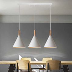 three pendant lights hanging over a dining room table with four chairs in front of it