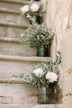 three vases filled with white flowers sitting on the side of some stone steps next to each other