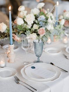 the table is set with white and blue plates, silverware, and floral centerpieces