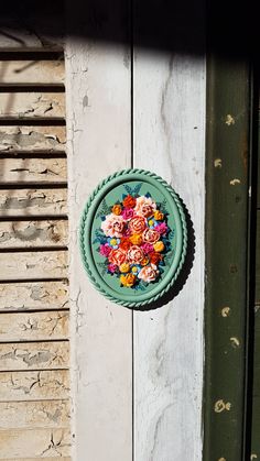 a green plate with flowers on it hanging from the side of a wooden wall next to a door