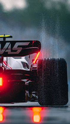 the front end of a racing car with its lights on and rain pouring over it