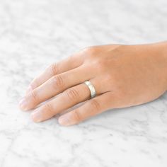 a person's hand with a wedding ring on top of their finger, resting on a marble surface