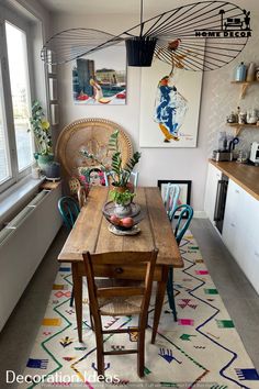 a dining room table with chairs and artwork on the wall above it in front of a window